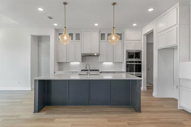 a large kitchen with granite countertop a large kitchen island white cabinetry and wooden floor