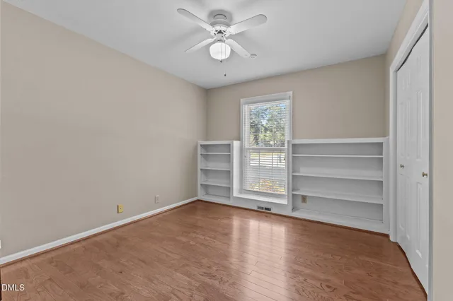 a view of an empty room with wooden floor and a ceiling fan