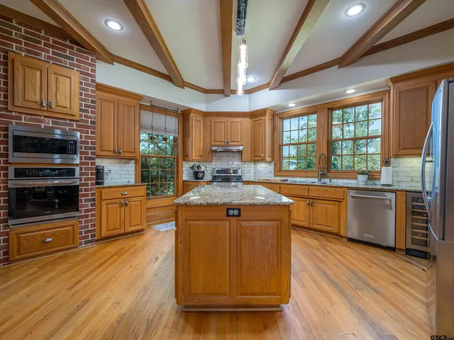 a kitchen with stainless steel appliances granite countertop wooden cabinets a refrigerator a sink a stove and a wooden floors