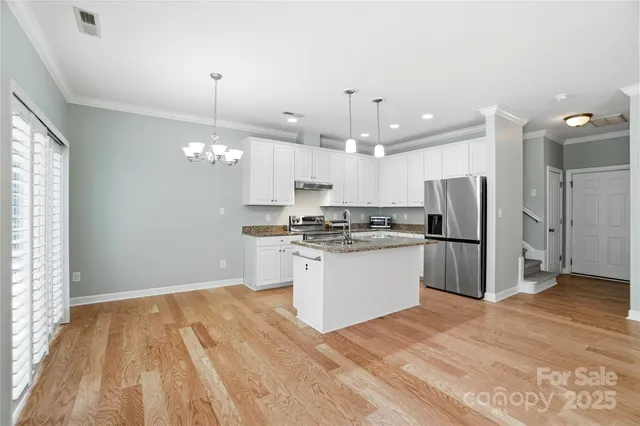 a kitchen with stainless steel appliances kitchen island granite countertop a refrigerator a sink dishwasher a stove and white cabinets with wooden floor