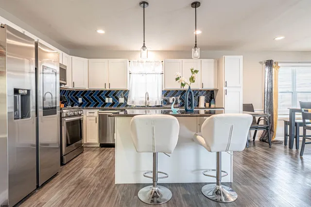 a kitchen with stainless steel appliances granite countertop a refrigerator a stove a sink dishwasher a dining table and chairs with wooden floor