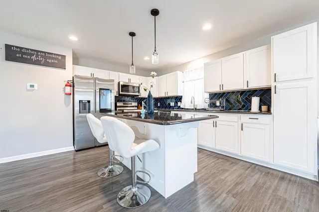 a kitchen with stainless steel appliances kitchen island granite countertop a refrigerator a white stove top oven a dining table and chairs with wooden floor