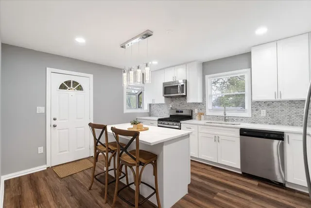 a kitchen with stainless steel appliances granite countertop a stove top oven a sink dishwasher a dining table and chairs with wooden floor