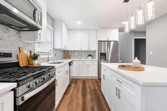 a kitchen with stainless steel appliances a stove a sink dishwasher a refrigerator and white cabinets with wooden floor