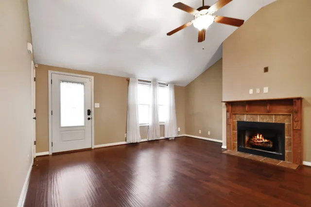 a view of an empty room with wooden floor fireplace and a window