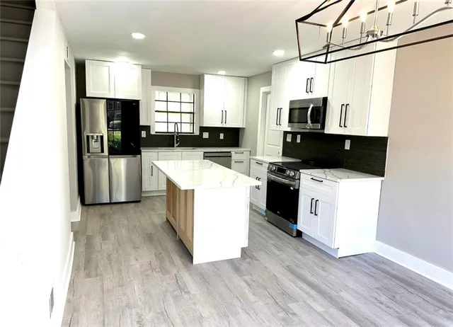 a kitchen with stainless steel appliances a stove top oven a sink a refrigerator white cabinets and wooden floor