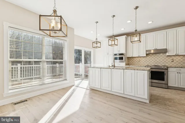a kitchen with granite countertop a stove a sink and white cabinets with wooden floor