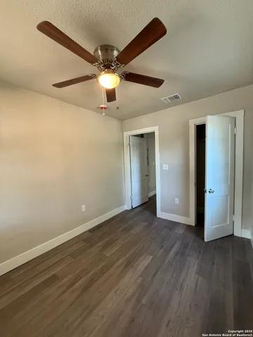a view of an empty room with wooden floor and a ceiling fan