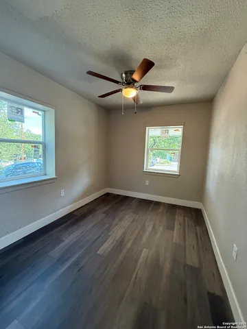 an empty room with wooden floor ceiling fan and windows