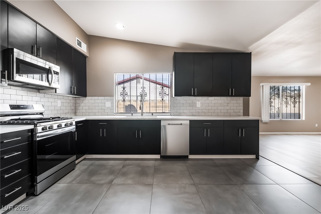 2246 East Russell Road Las Vegas, NV 89119 - Photo 2 of 24 Kitchen featuring dark cabinetry, appliances with stainless steel finishes, tasteful backsplash, light tile patterned flooring, and light stone counters