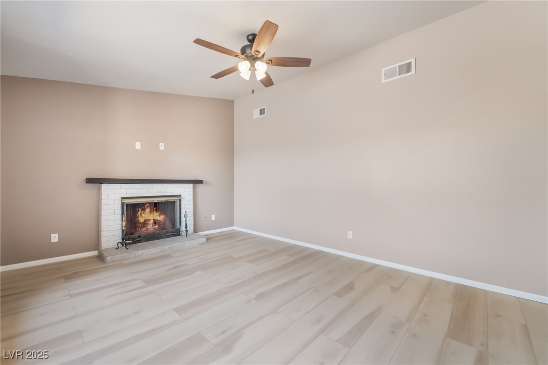 2246 East Russell Road Las Vegas, NV 89119 - Photo 3 of 24 Unfurnished living room featuring light wood-style floors, a fireplace, and ceiling fan