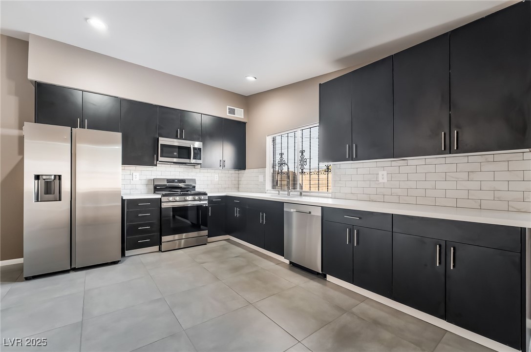 2246 East Russell Road Las Vegas, NV 89119 - Photo 8 of 24 Kitchen with dark cabinetry, appliances with stainless steel finishes, decorative backsplash, light tile patterned floors, and light stone countertops