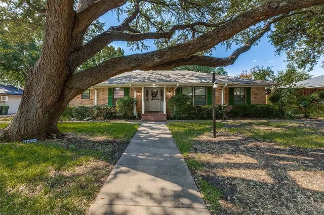 a view of a white house with a big yard and potted plants and large trees