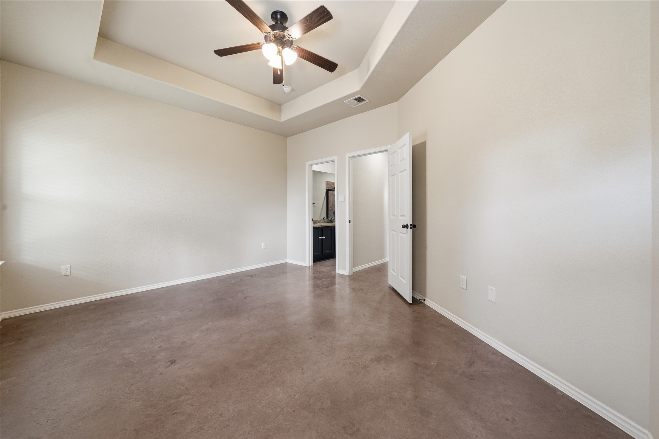 533 Jack Rabbit Lane, Unit A Buda, TX 78610 - Photo 23 of 34 A spacious bedroom features a ceiling fan, tray ceiling, and concrete flooring.