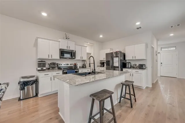 a kitchen with stainless steel appliances granite countertop a refrigerator a stove top oven a sink dishwasher and white cabinets with wooden floor
