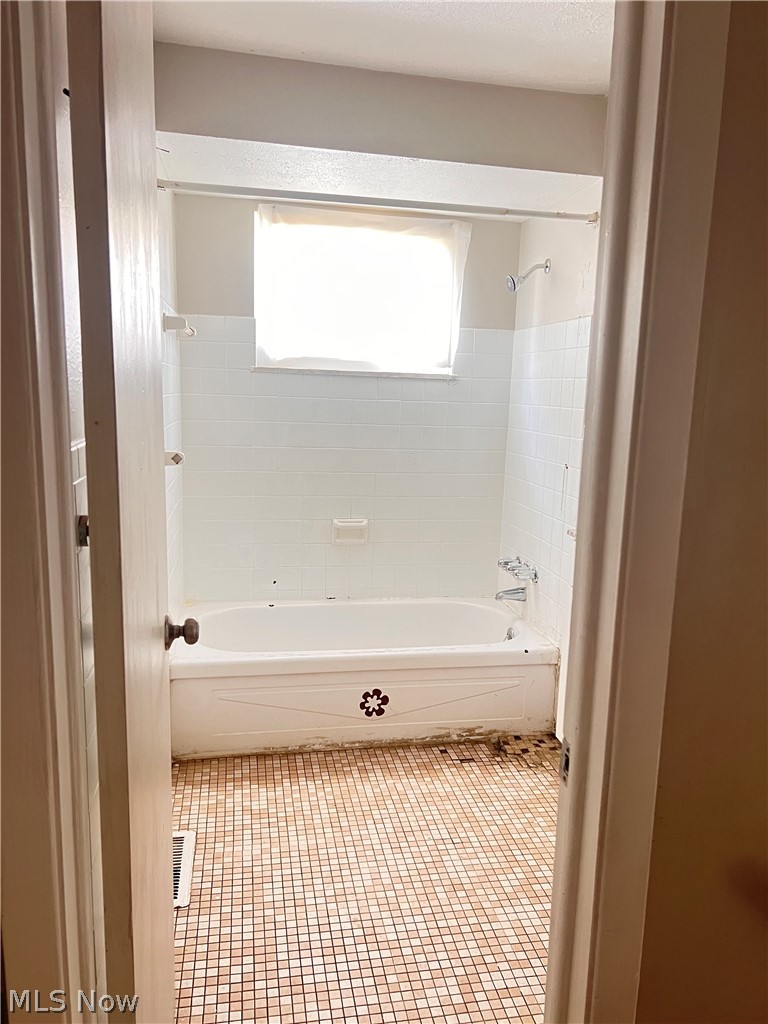 16350 Rockside Road Maple Heights, OH 44137 - Photo 14 of 34 Bathroom featuring a white bathtub with a decorative panel, white subway tile surround, and a window