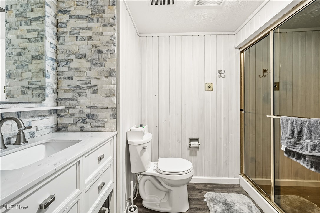 8193 Hartman Road Wadsworth, OH 44281 - Photo 31 of 50 Full bathroom with dark wood-style flooring, vanity, a stall shower, wooden walls, and a textured ceiling