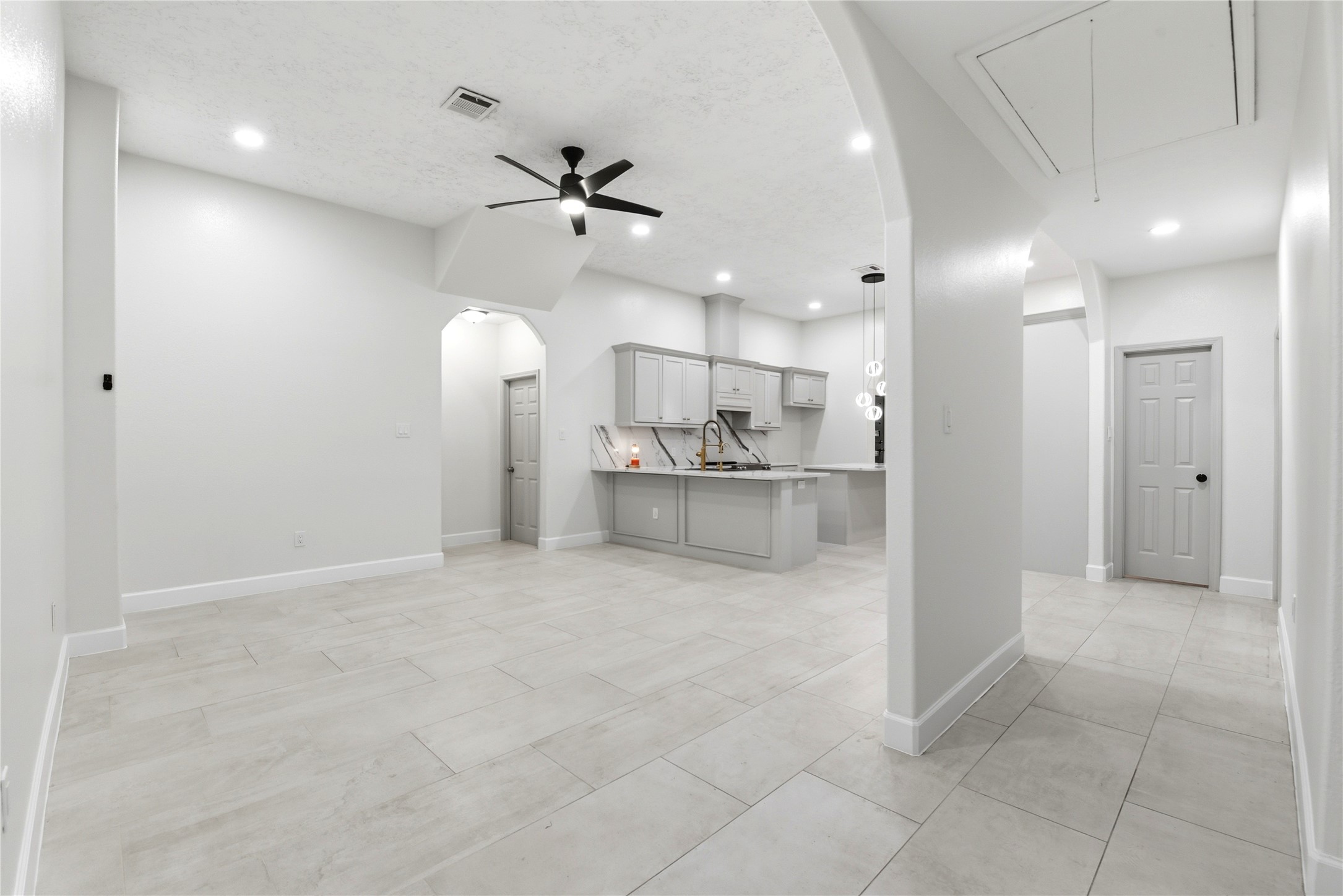 9403 Spaulding Street Houston, TX 77016 - Photo 8 of 50 This photo showcases a spacious, modern open-concept living area with light tile flooring and neutral walls. The kitchen features sleek cabinetry, a center island with pendant lighting, and built-in appliances. Ceiling fans and recessed lighting add to the contemporary feel.