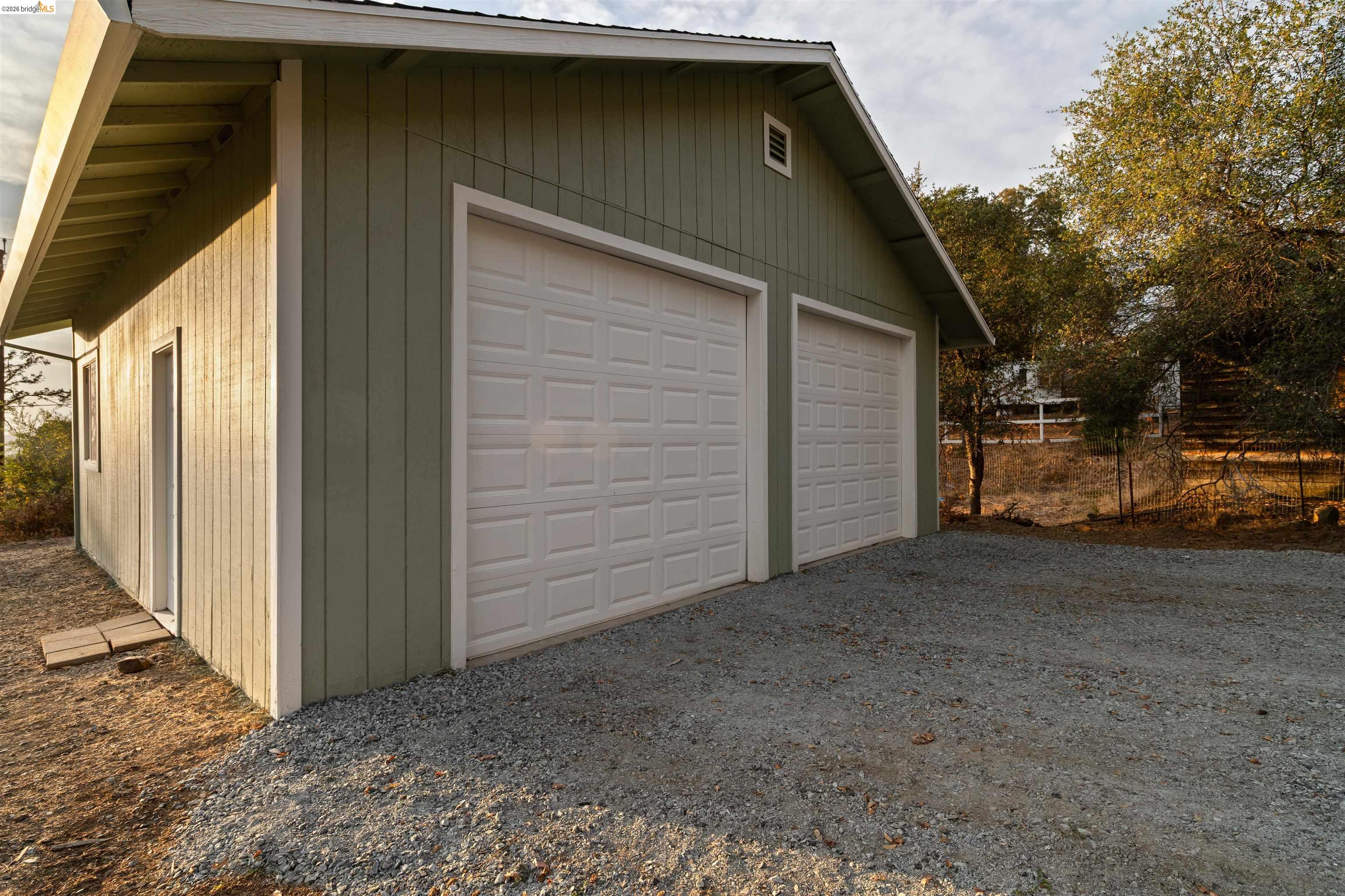 19676 Rawhide Road Sonora, CA 95370 - Photo 54 of 67 Two-car garage with panel-style doors, board and batten siding, and a gravel driveway