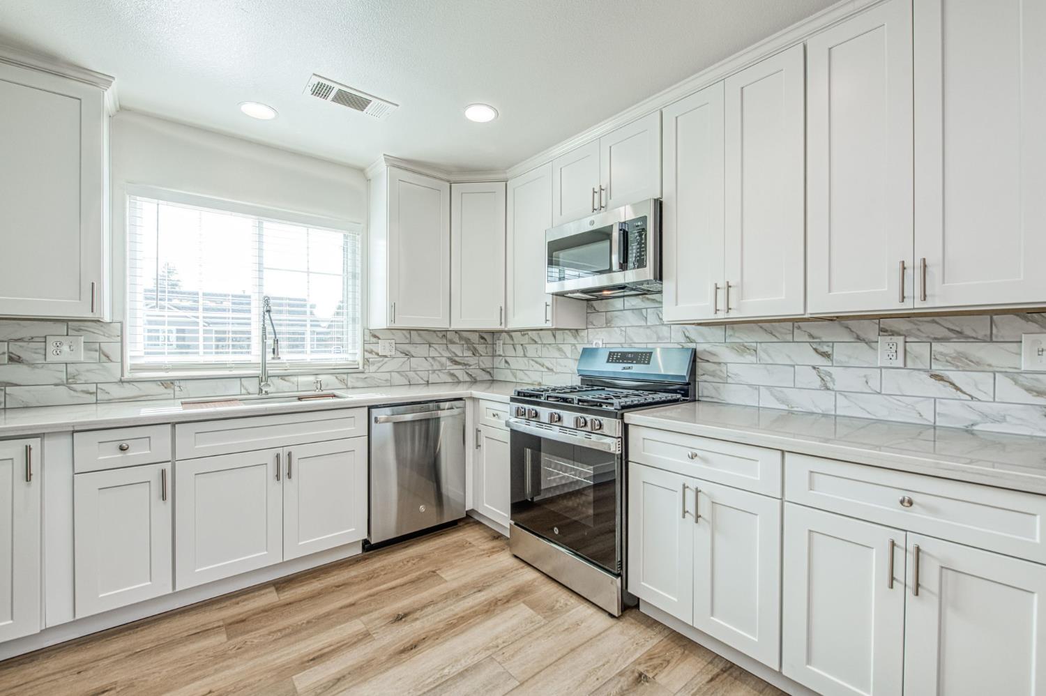 5176 West Michigan Avenue Fresno, CA 93722 - Photo 29 of 37 a kitchen with granite countertop white cabinets white stainless steel appliances a sink and a window