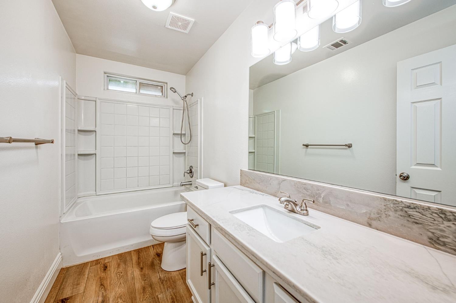 5176 West Michigan Avenue Fresno, CA 93722 - Photo 6 of 37 a bathroom with a granite countertop sink a toilet a mirror and shower