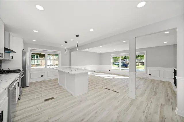 a large kitchen with kitchen island a stove a sink dishwasher a refrigerator and white cabinets with wooden floor