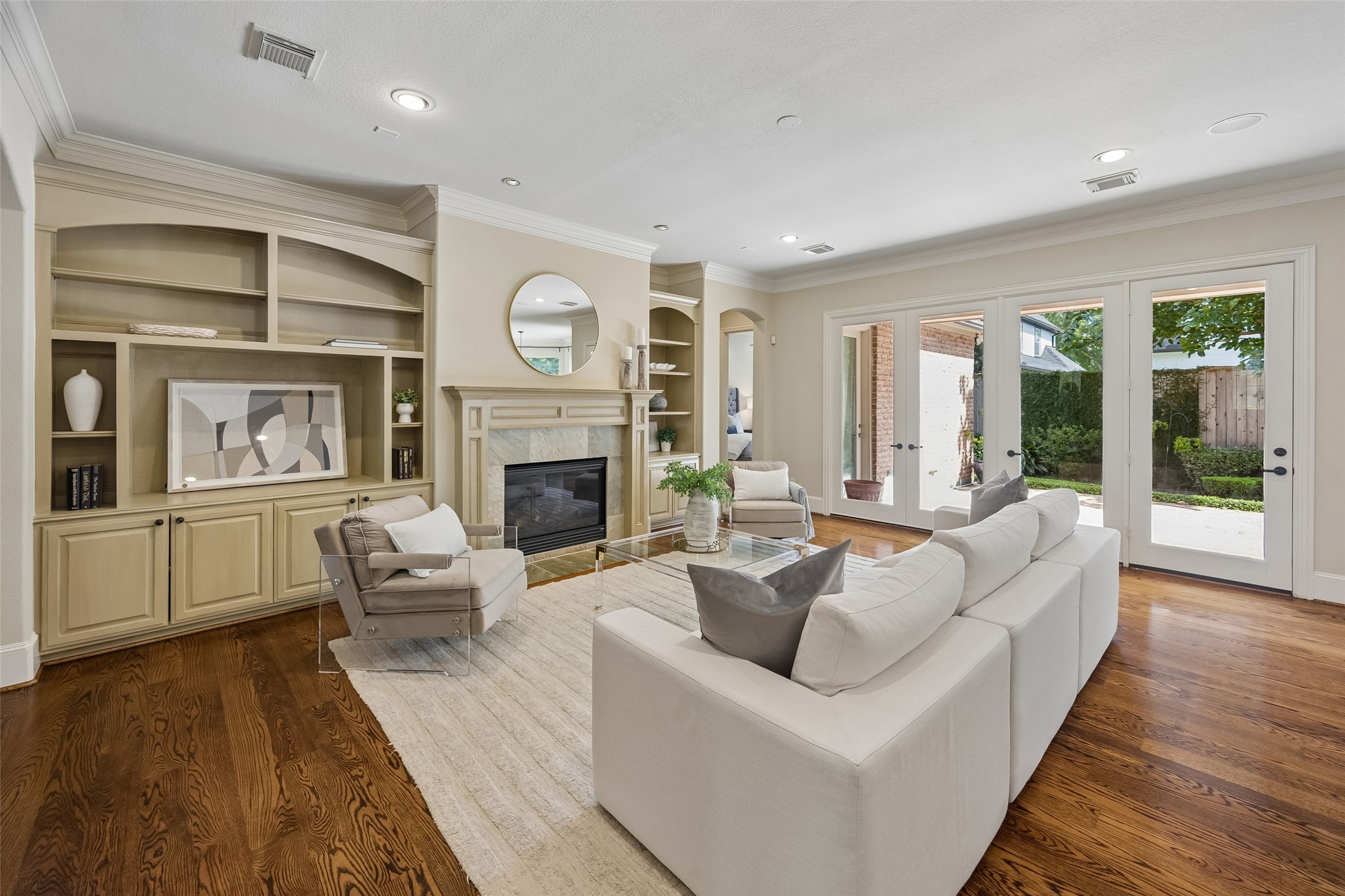 Bright and inviting living room with elegant built-in shelving, a cozy fireplace, and abundant natural light from French doors opening to the backyard.