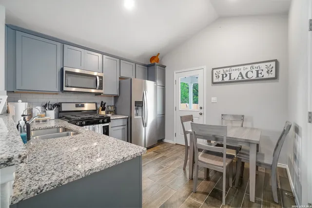 a kitchen with stainless steel appliances granite countertop a stove a refrigerator a sink a dining table and chairs