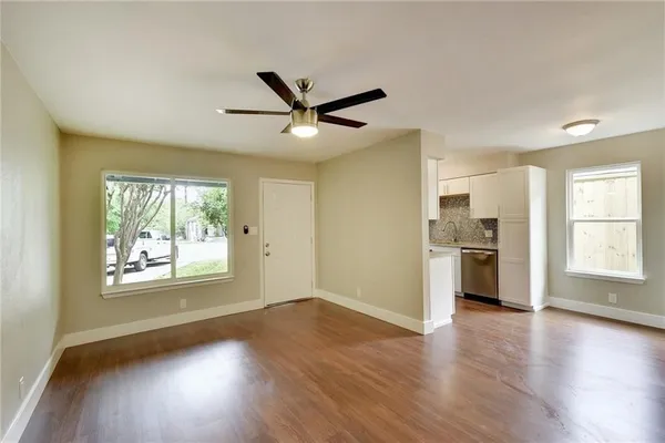 a view of a kitchen and an empty room with wooden floor and a window