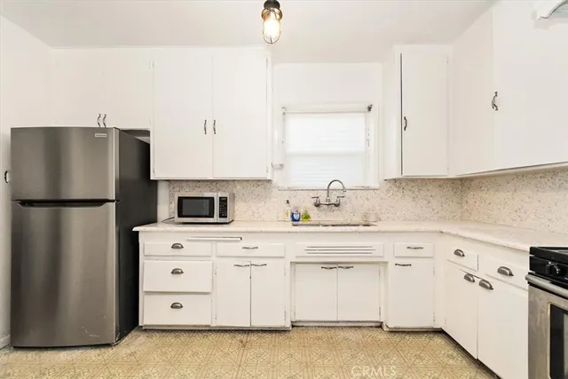 a kitchen with granite countertop a refrigerator sink stove and white cabinets