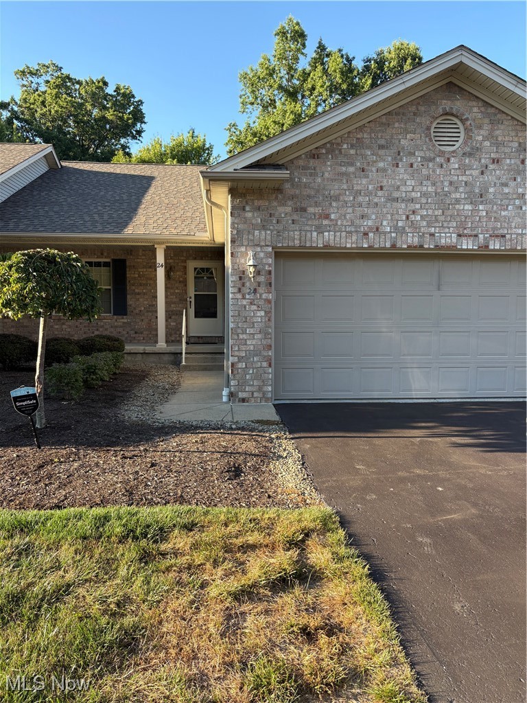 Ranch-style house featuring covered porch, asphalt driveway, an attached garage, brick siding, and roof with shingles