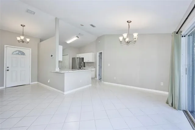 an empty room with kitchen view and a chandelier