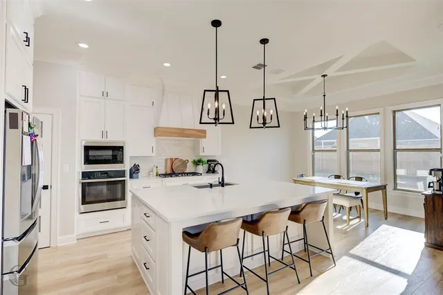 a kitchen with stainless steel appliances a stove a sink a oven a kitchen island with a stove and white cabinets