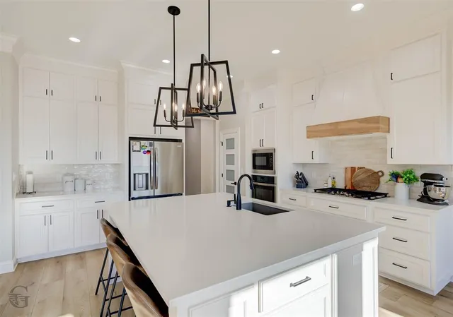 a kitchen with stainless steel appliances a sink a stove a refrigerator a center island and cabinets