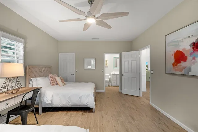 a bedroom with a bed and a lamp on dresser with wooden floor