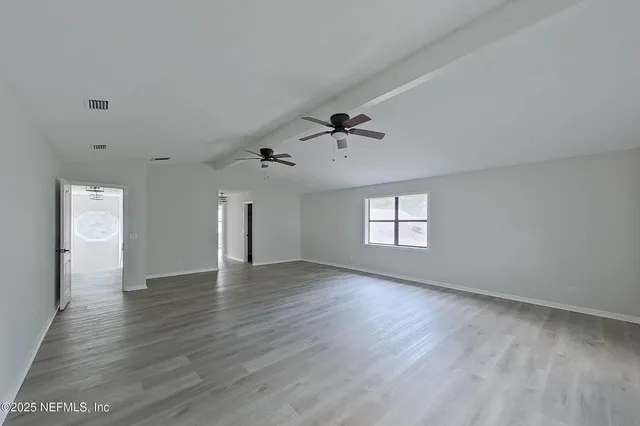 a view of an empty room with window and wooden floor