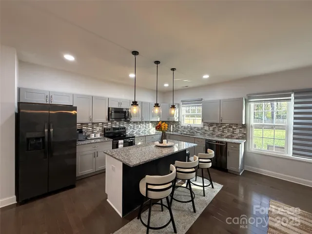 a kitchen with stainless steel appliances granite countertop a stove a refrigerator a sink a dining table and chairs