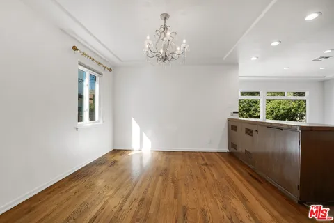 a view of an empty room with wooden floor and a kitchen