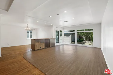 a view of an empty room with wooden floor and kitchen view