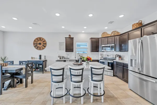 a kitchen with stainless steel appliances granite countertop a refrigerator and a dining table with wooden floor