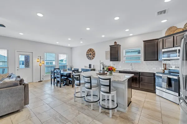 a very nice looking open dining room kitchen with stainless steel appliances granite countertop a stove a sink a dining table and chairs