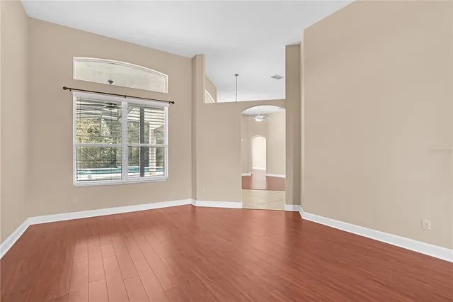 an empty room with wooden floor chandelier and windows