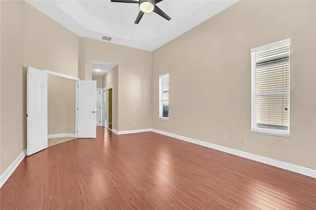 an empty room with wooden floor chandelier fan and windows