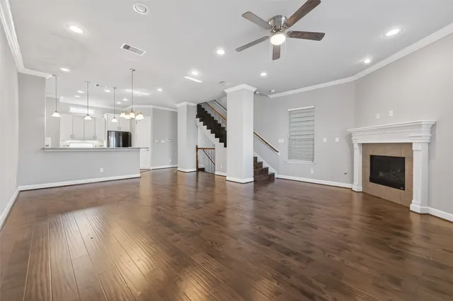 an empty room with wooden floor a ceiling fan and kitchen view