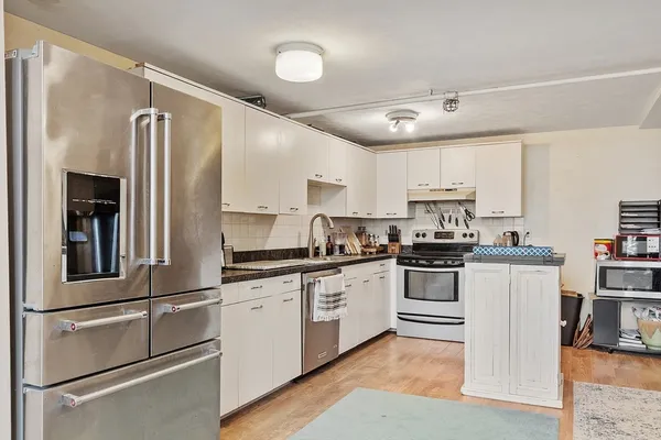 a kitchen with stainless steel appliances granite countertop a refrigerator a stove and a sink with wooden floor