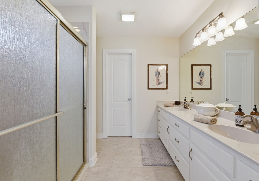 232 North Dixie Street Brenham, TX 77833 - Photo 28 of 41 This bathroom features a double vanity with ample storage, a large mirror, and elegant lighting. It includes a sliding glass door shower and neutral tile flooring, creating a clean and spacious ambience.