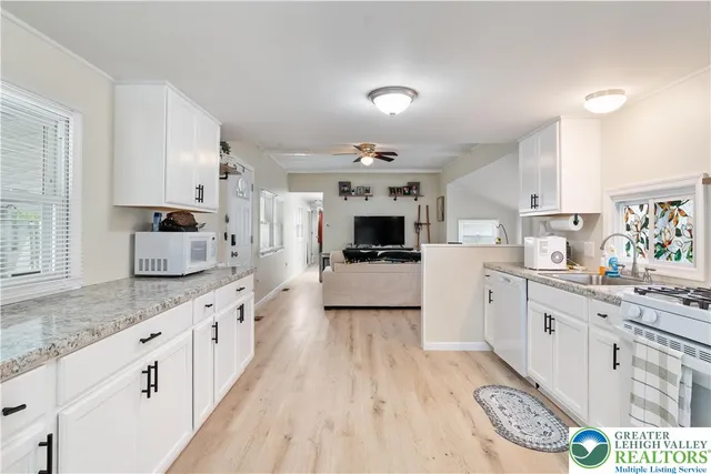 a kitchen with granite countertop a sink dishwasher stove and white cabinets with wooden floor