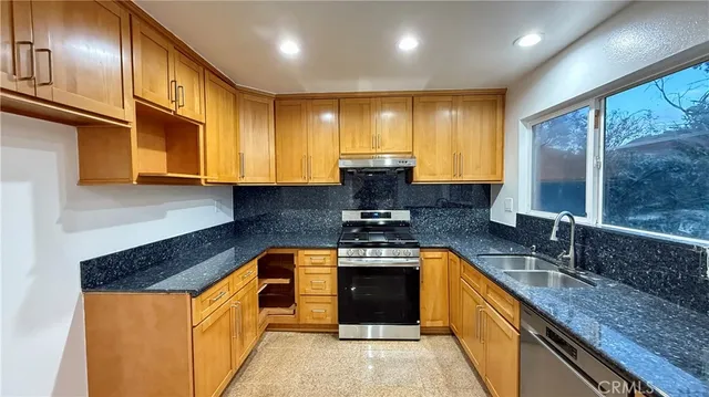 a kitchen with stainless steel appliances granite countertop a sink a stove and a wooden cabinets