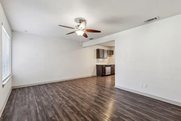an empty room with wooden floor chandelier fan and windows