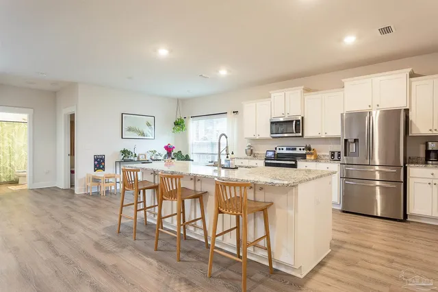 a kitchen with stainless steel appliances a refrigerator a stove a sink dishwasher and a dining table with wooden floor